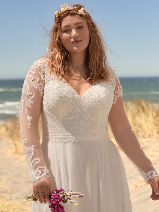 Curvy Frau trägt Brautkleid mit langen Ärmeln am Strand